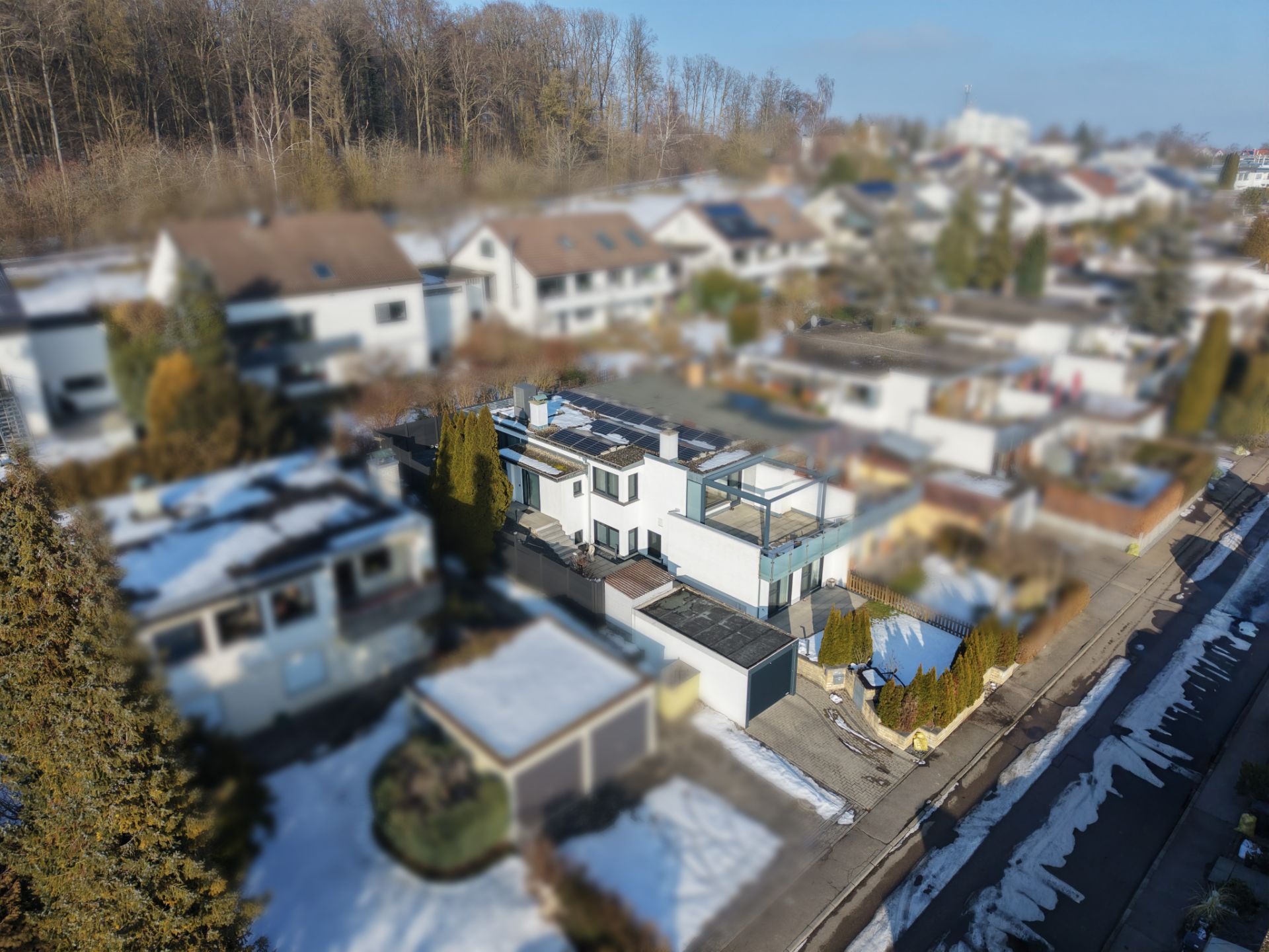 Luftaufnahme eines modernen Wohnhauses mit Garage und Garten, umgeben von weiteren Häusern.