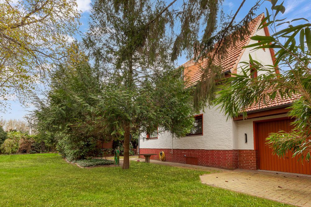 Haus mit rotem Dach, Garten, Bäumen und Garage, grüne Wiese im Vordergrund.
