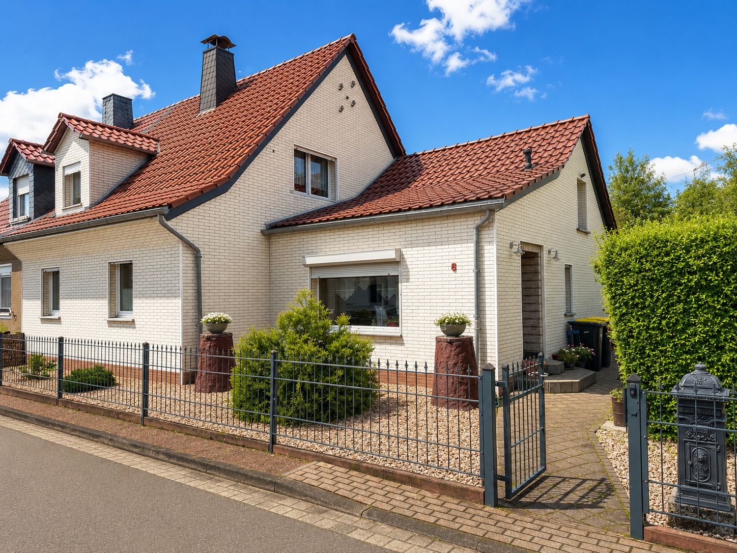 Zweistöckiges Wohnhaus mit rotem Dach, weißer Fassade und kleinem Vorgarten hinter einem Zaun.