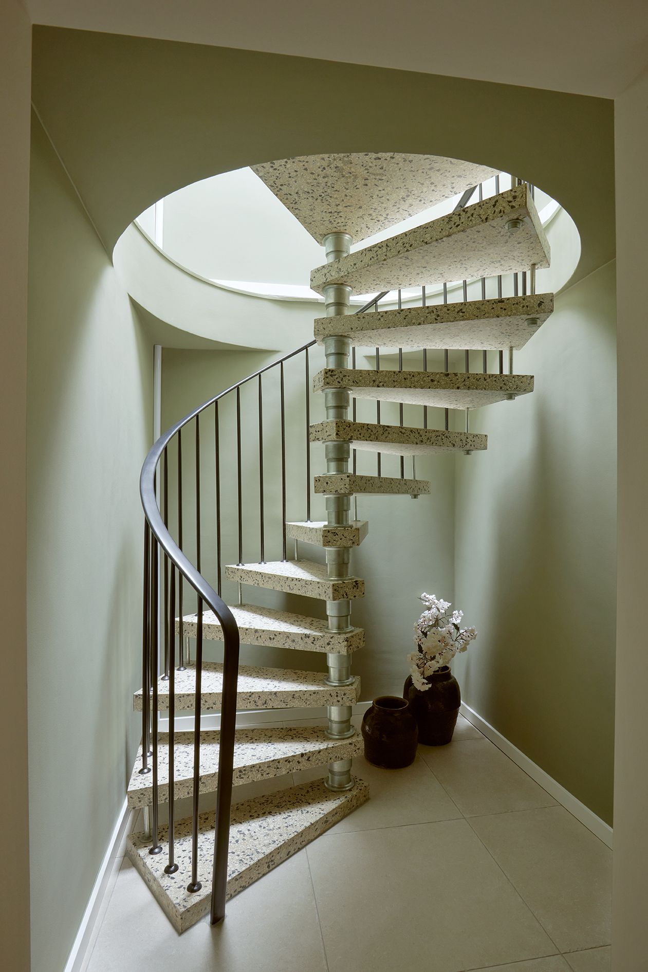 Moderne Wendeltreppe mit Terrazzo-Stufen, daneben zwei Vasen mit Zweigen in einer hellen Ecke.