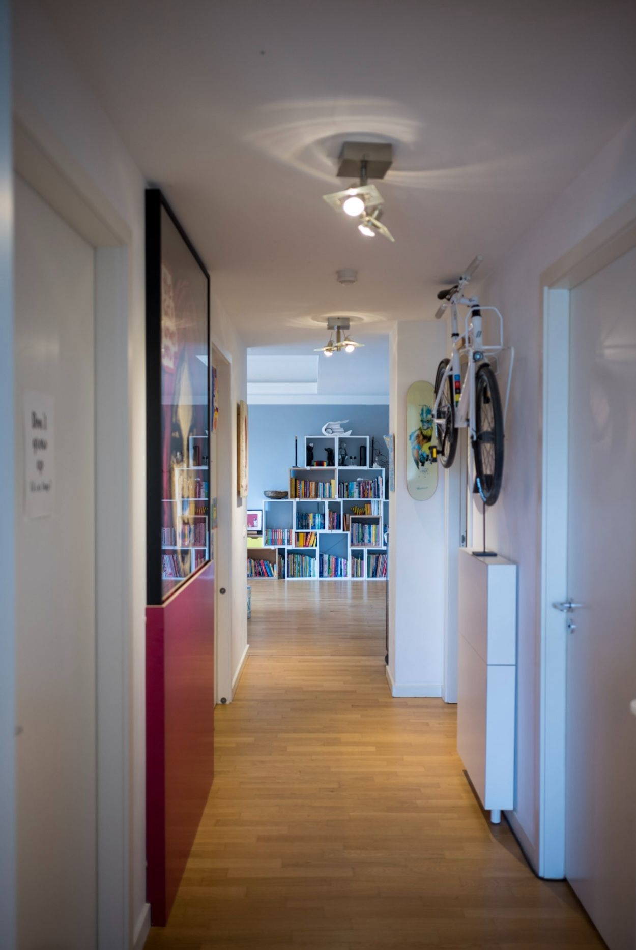 Heller Flur mit Holzfußboden, Wandfahrradhalter und Bücherregal im Hintergrund.