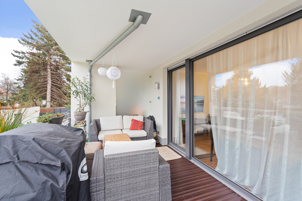 Moderne Terrasse mit Sitzgruppe, Tisch, Grill und Pflanzkübeln vor Glas-Schiebetür.