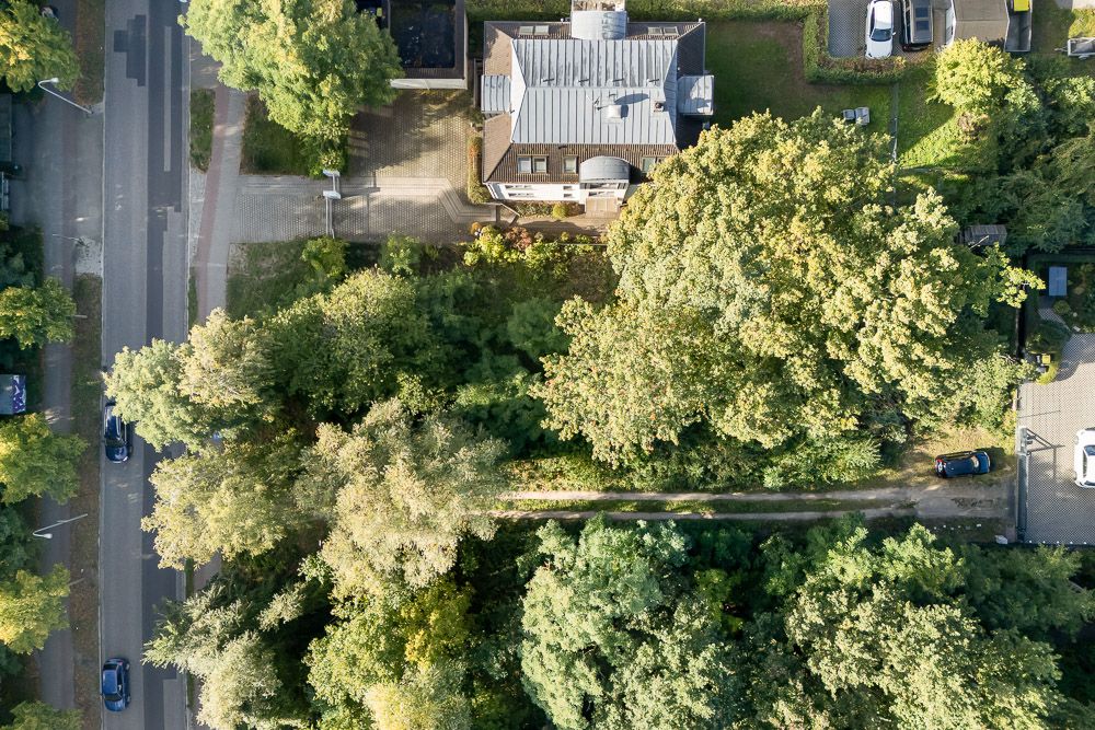 Luftaufnahme eines Wohnhauses mit Garten, umgeben von vielen Bäumen, neben einer Straße.