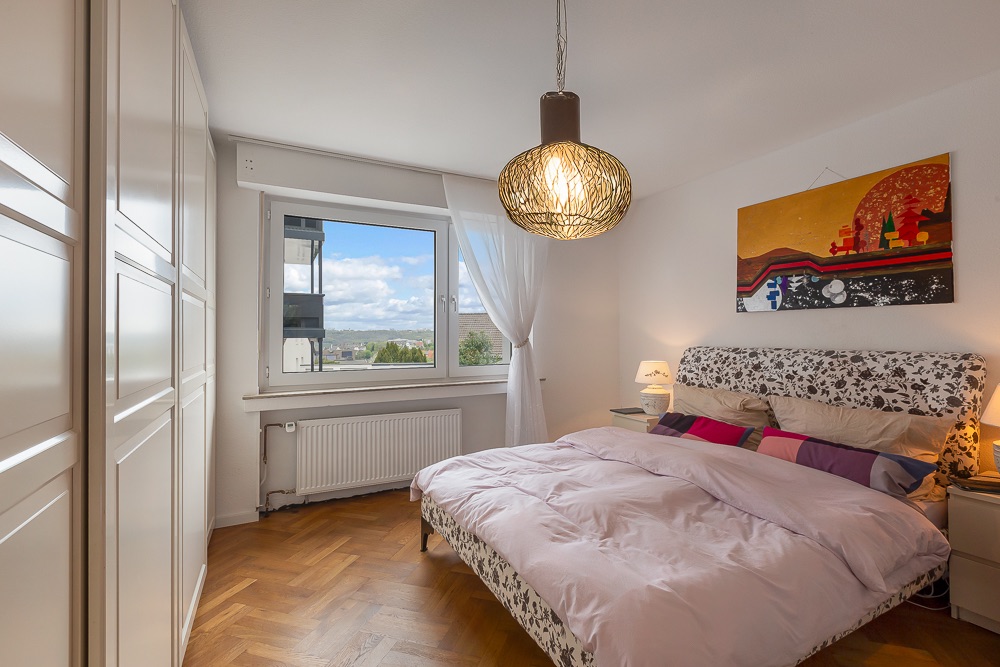 Helles Schlafzimmer mit Doppelbett, großem Kleiderschrank, Fenster und bunter Wandkunst.