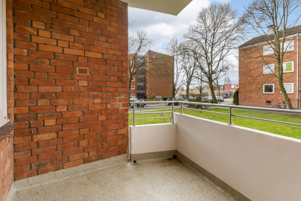 Balkon mit Backsteinwand, Metallgeländer und Blick auf Rasen sowie Wohngebäude.