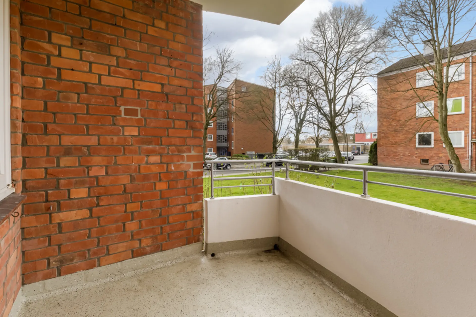 Balkon mit Backsteinwand, Metallgeländer und Blick auf Rasen sowie Wohngebäude.