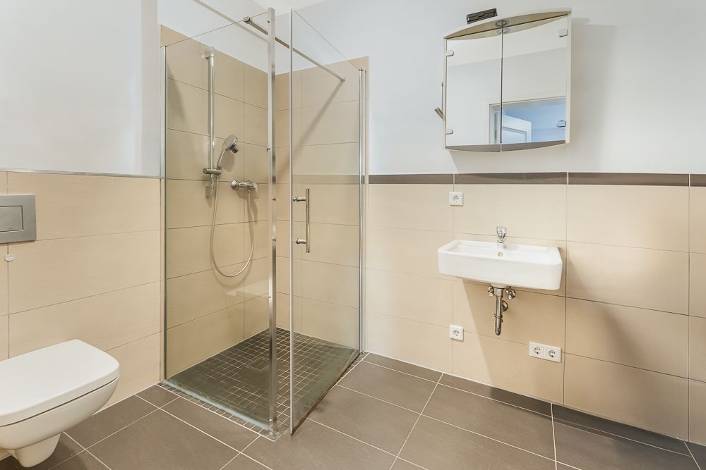 Modernes Badezimmer mit bodengleicher Dusche, Wandtoilette, Waschbecken und Spiegelschrank.