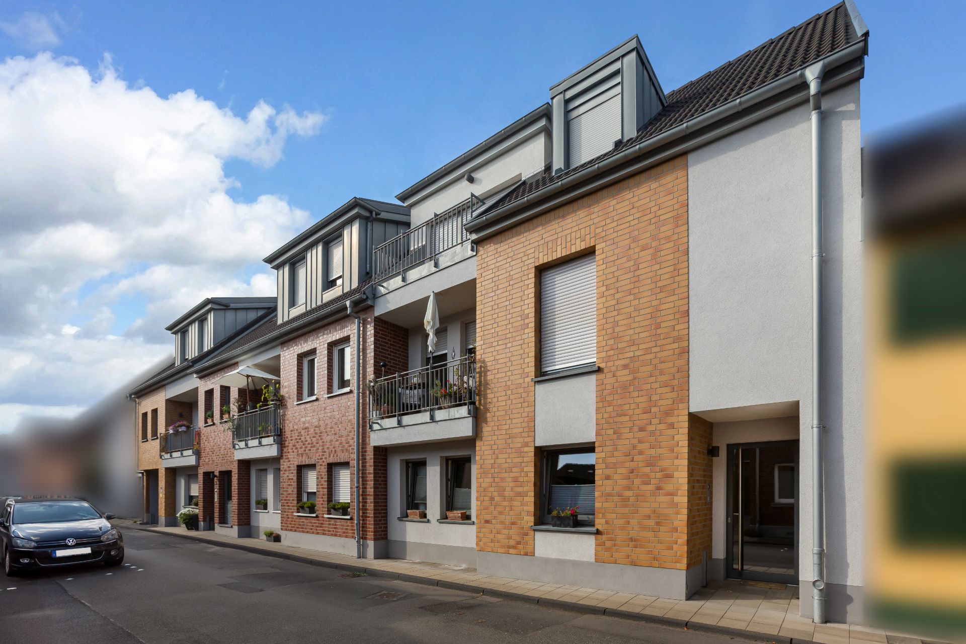 Mehrfamilienhaus mit Backsteinfassade, Balkonen und geparktem Auto auf ruhiger Straße.