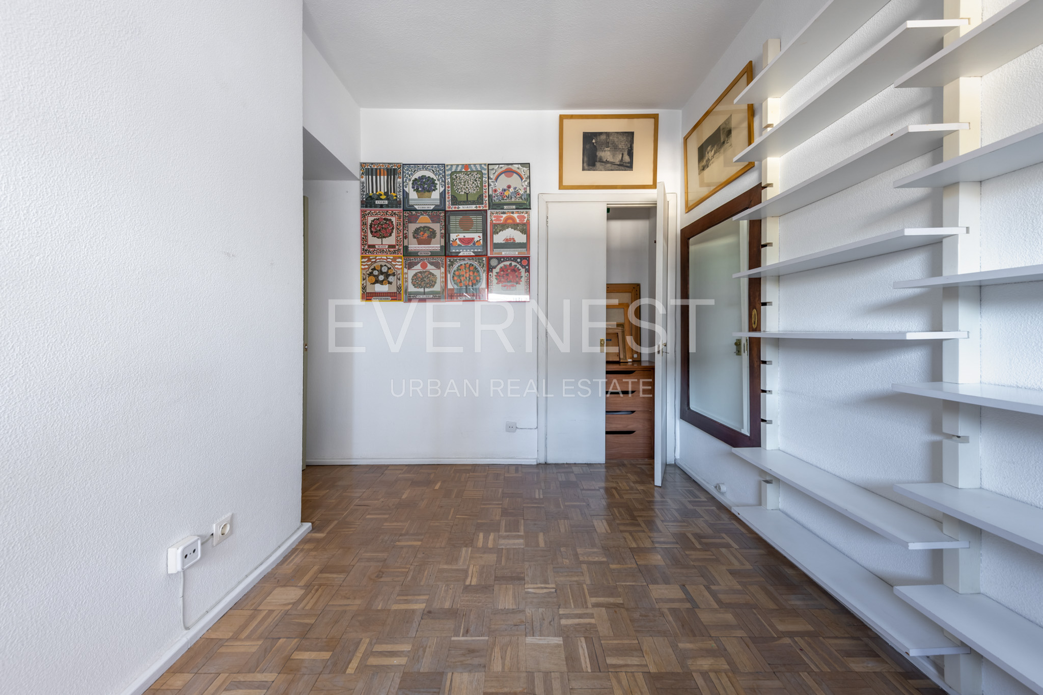 Heller Raum mit Parkettboden, weißen Wandregalen und dekorativen Bildern an der Wand.