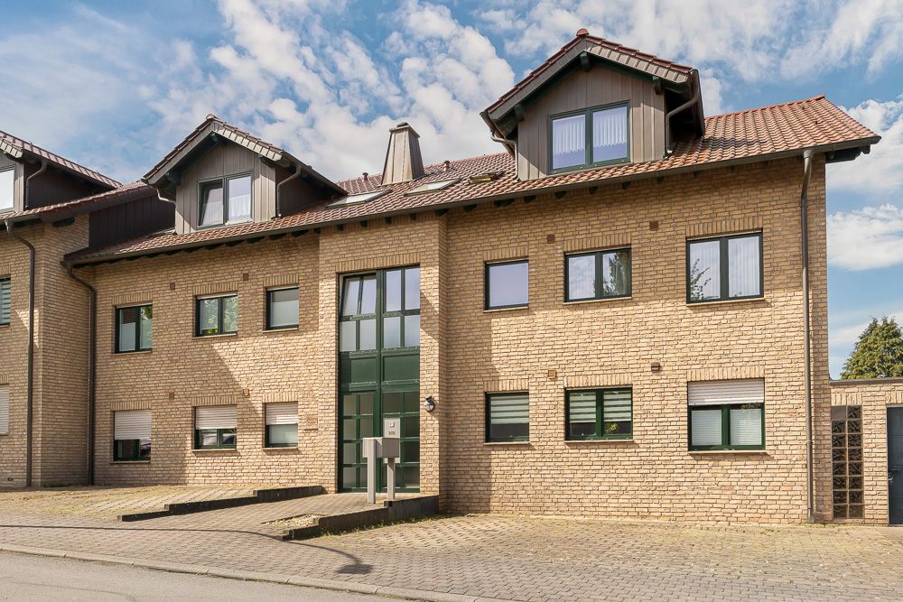 Zweistöckiges Wohnhaus aus Backstein mit mehreren Fenstern und Dachgauben, Zufahrt und Eingangstür sichtbar.