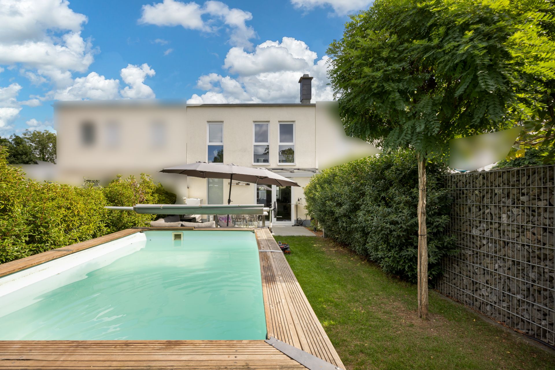 Moderner Garten mit rechteckigem Pool, Holzdeck, Sonnenschirm und angrenzendem Wohnhaus.