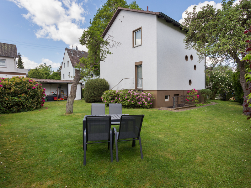 Ein Garten mit vier Gartenstühlen und einem Tisch vor einem weißen Wohnhaus.