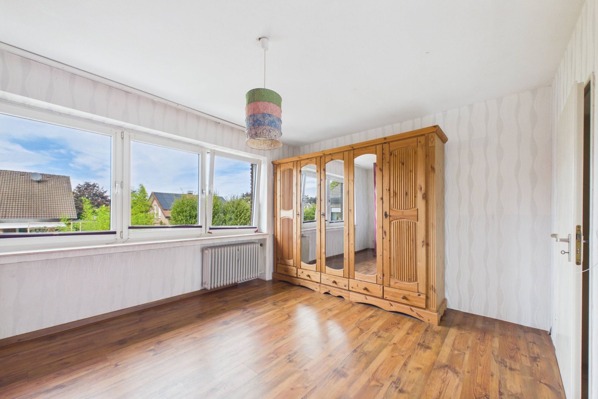 Helles Zimmer mit Holzschrank, großem Fenster und Holzboden.