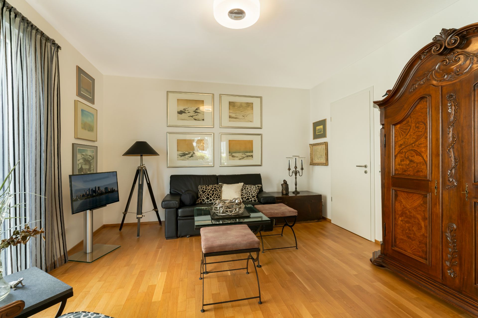 Wohnzimmer mit schwarzem Sofa, Holzboden, großem Schrank und Wandbildern.