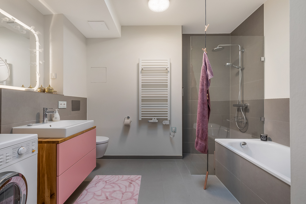 Modernes Badezimmer mit Waschmaschine, Badewanne, Dusche, Waschtisch und Handtuchheizkörper.