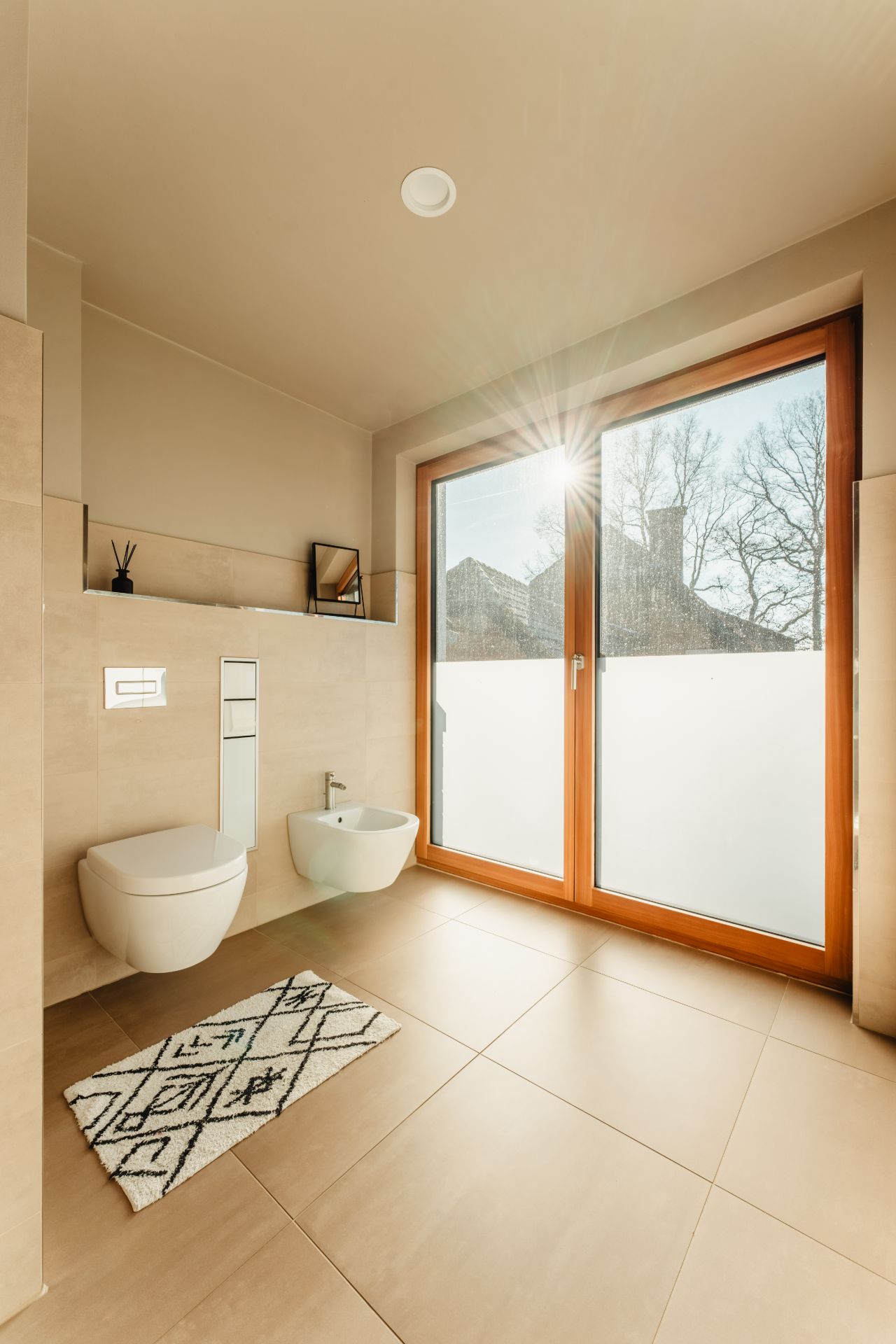 Modernes Badezimmer mit WC, Bidet, Teppich und großem Fenster mit Holzrahmen.