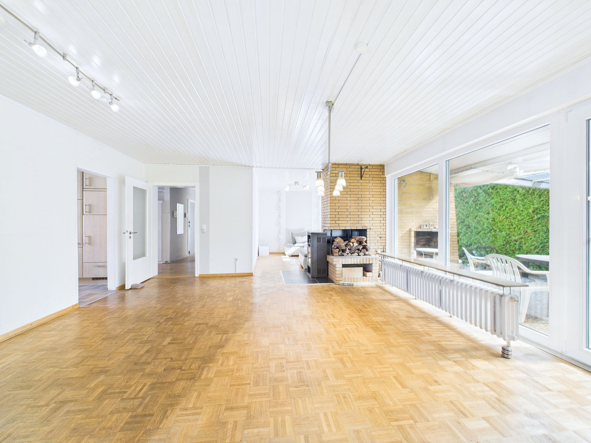 Helles Wohnzimmer mit Parkettboden, großen Fenstern und Kamin, angrenzend an eine Terrasse.