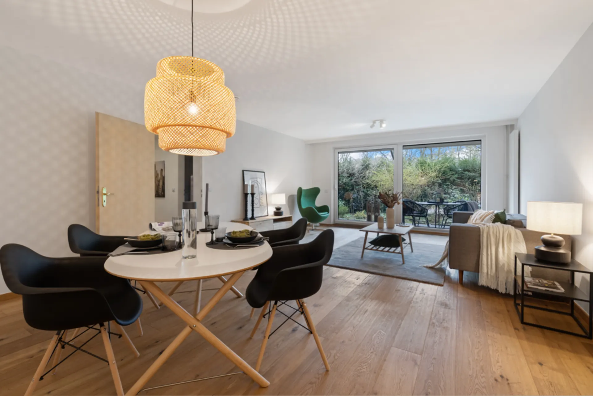 Modernes Wohnzimmer mit Esstisch, Sofa und großen Fenstern zum Garten.