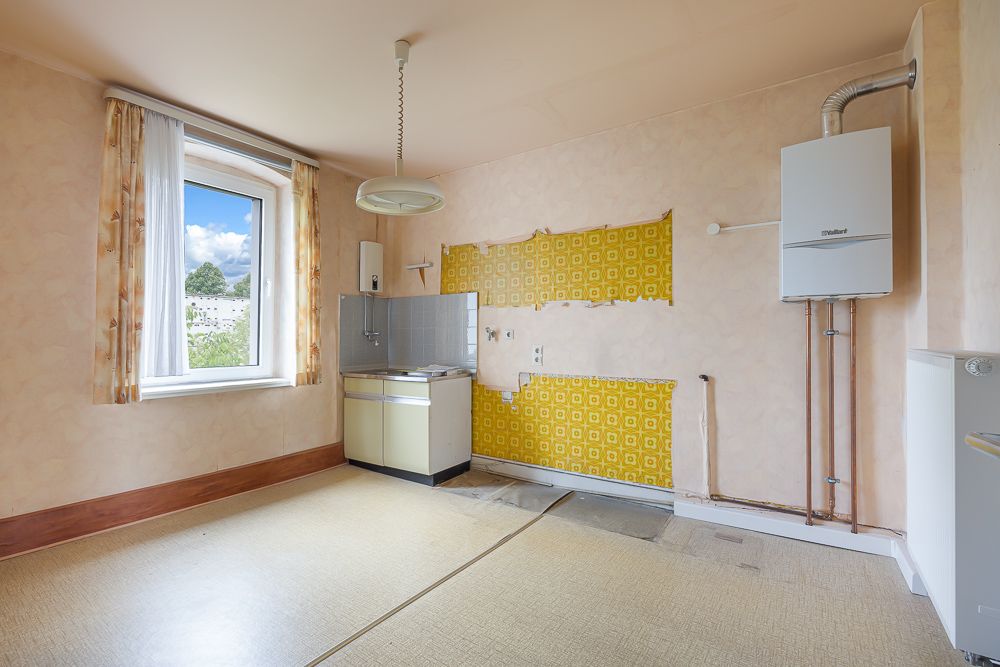 Leerer Raum mit kleinem Spülbecken, gelber Tapete und einem großen Fenster.