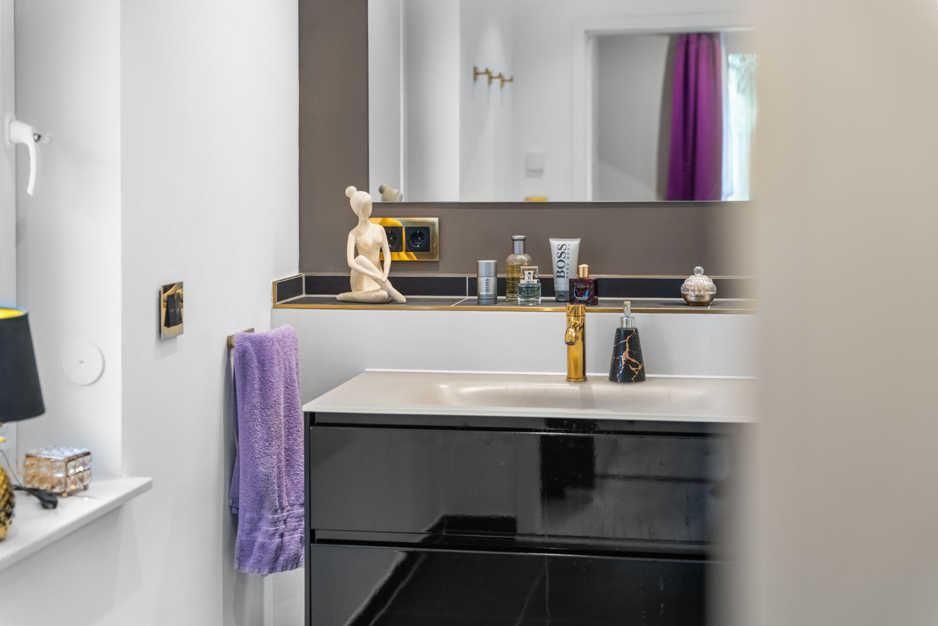 Modernes Bad mit schwarzem Waschbecken, Spiegel und lila Handtuch.
