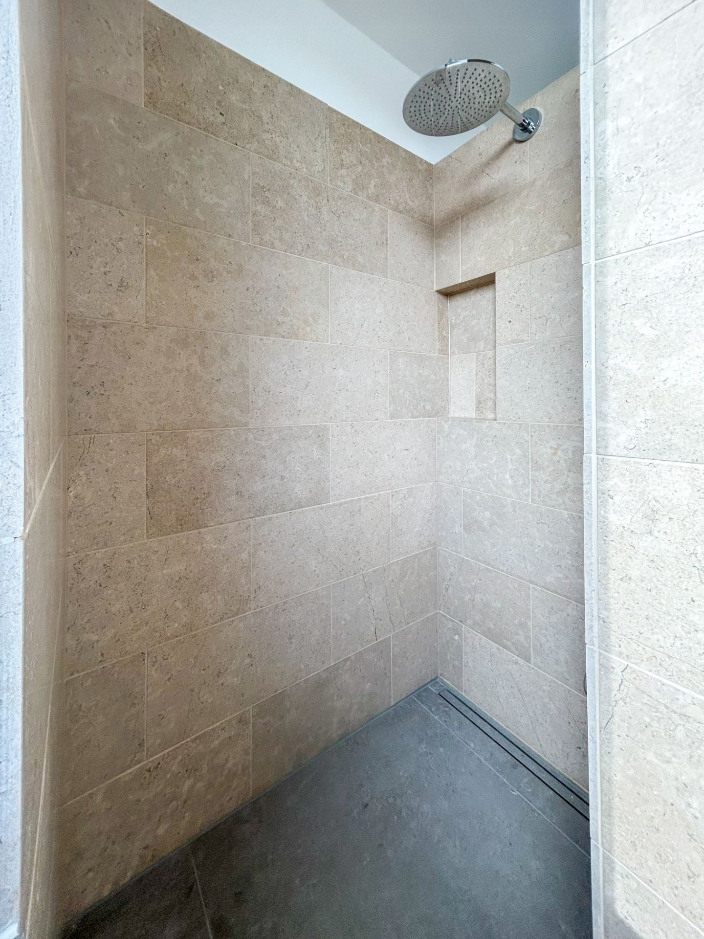 Begehbare Dusche mit beigen Fliesen und großer Regendusche.