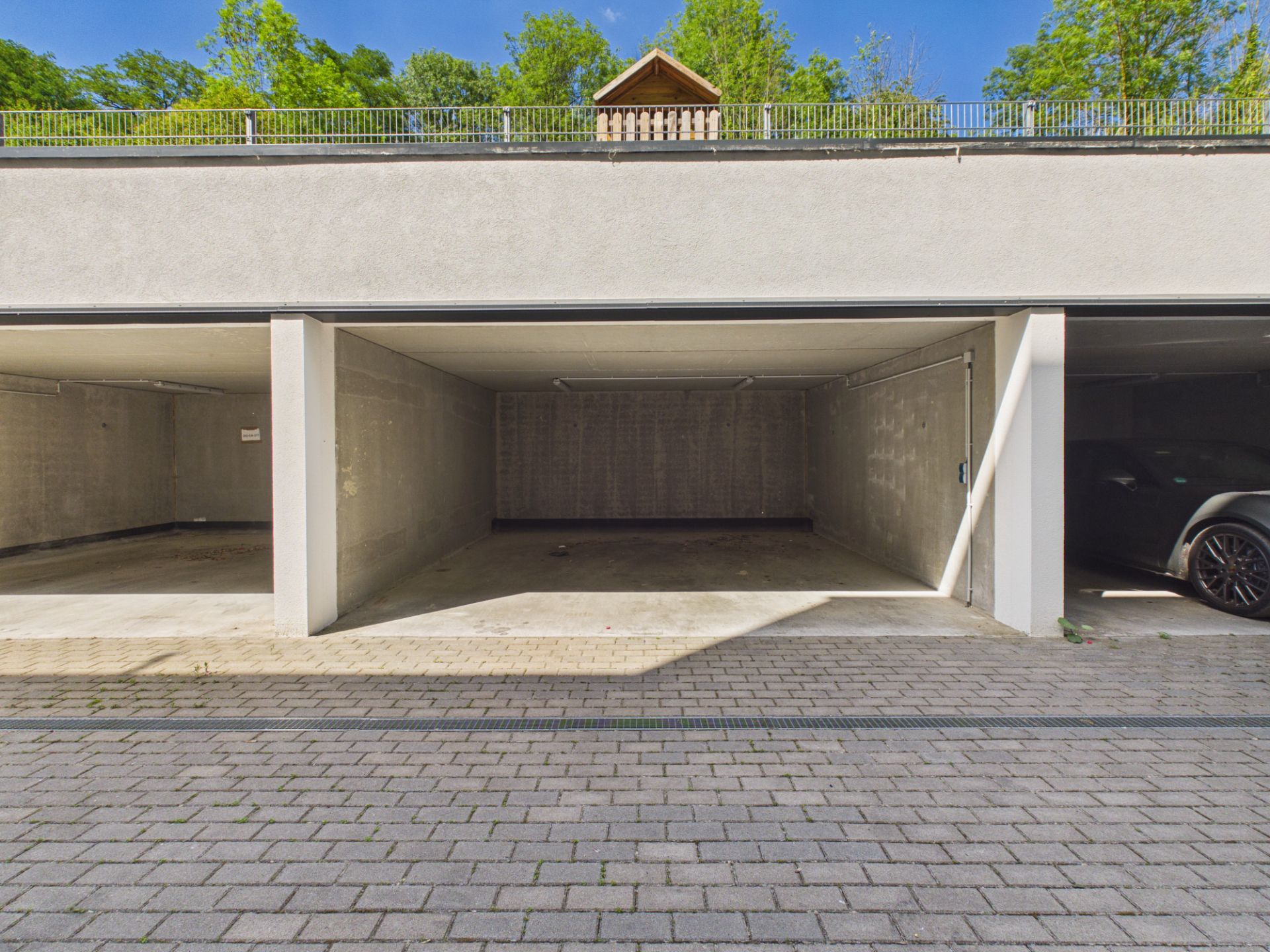 Leere, überdachte Stellplätze in einer offenen Garage, rechts ein parkendes Auto.