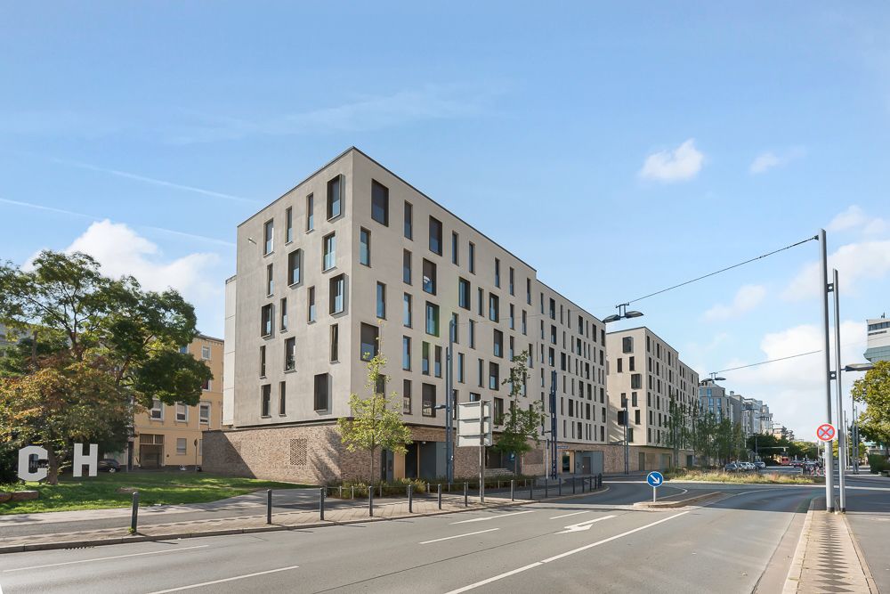 Mehrstöckiges Wohngebäude an einer Straße mit Bäumen und Gehweg.