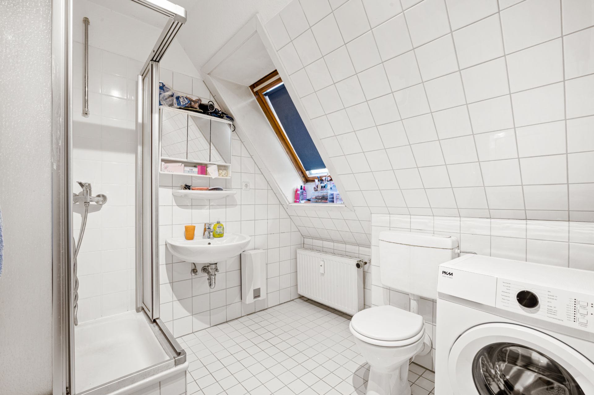 Helles Bad mit Dusche, Waschbecken, Toilette, Waschmaschine und Dachfenster.
