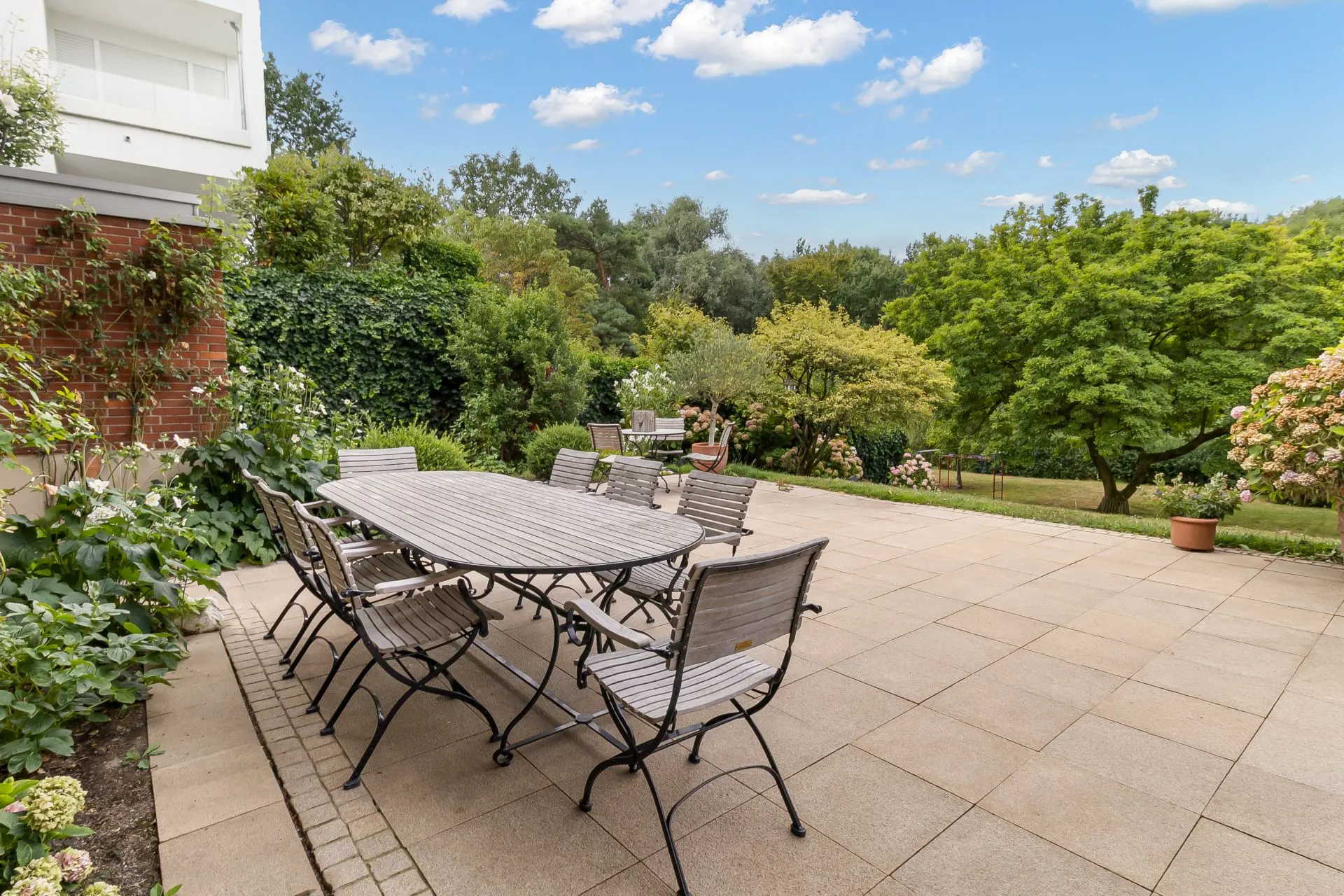 Große Terrasse mit Esstisch und Stühlen, umgeben von viel Grün und Bäumen.