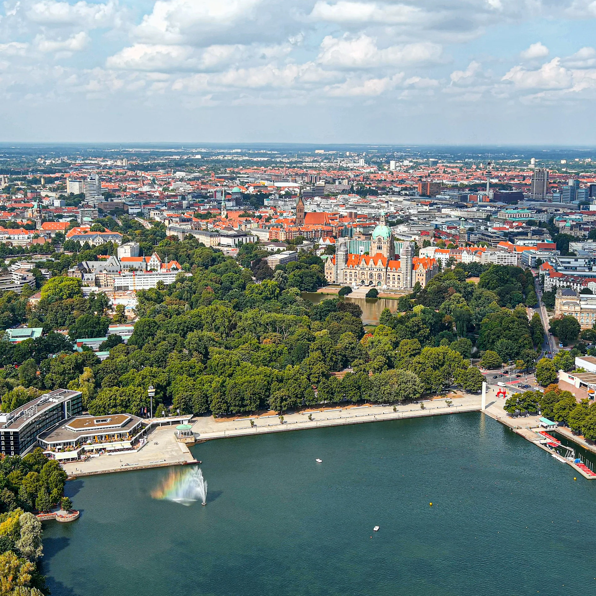 Luftaufnahme einer Stadt mit großem Teich, Springbrunnen und grünen Parkanlagen.