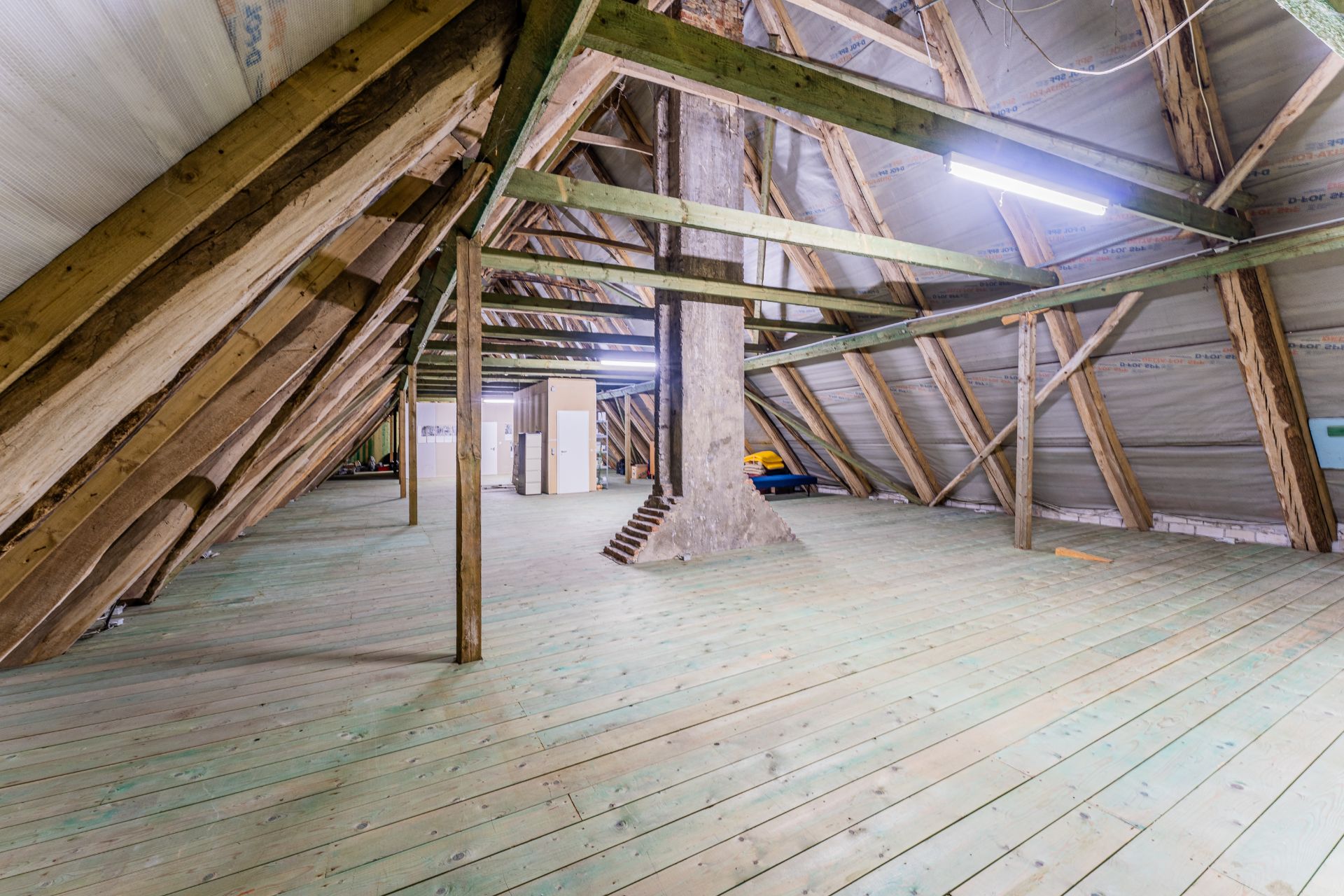 Dachboden mit Holzbalken, grünem Holzboden und sichtbarem Schornstein.