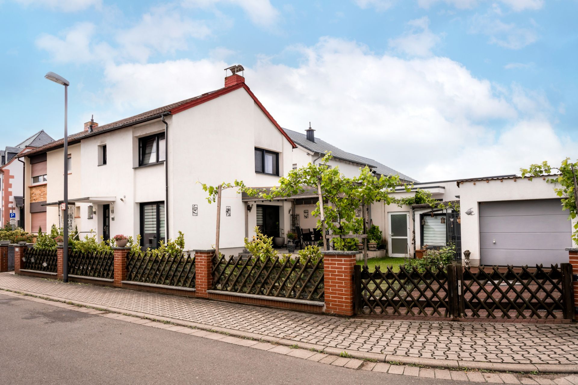 Zweistöckiges Wohnhaus mit Garten, Terrasse und Garage, von einem Zaun umgeben.