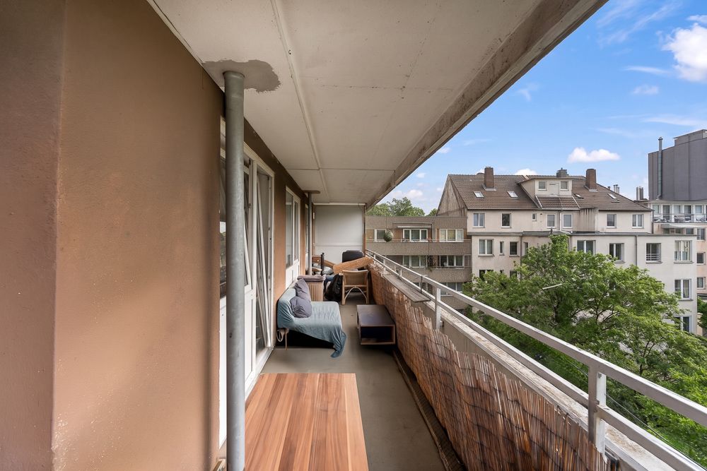 Langer Balkon mit Sitzmöbeln und Blick auf benachbarte Wohngebäude und Bäume.