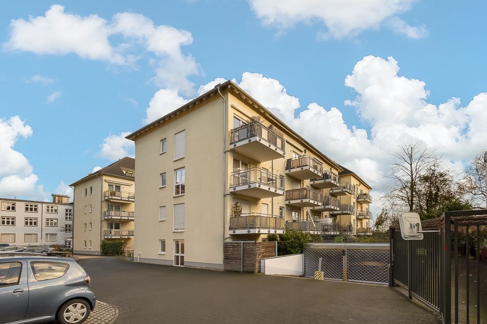 Mehrstöckiges Wohngebäude mit Balkonen und angrenzendem Parkplatz bei Tageslicht.