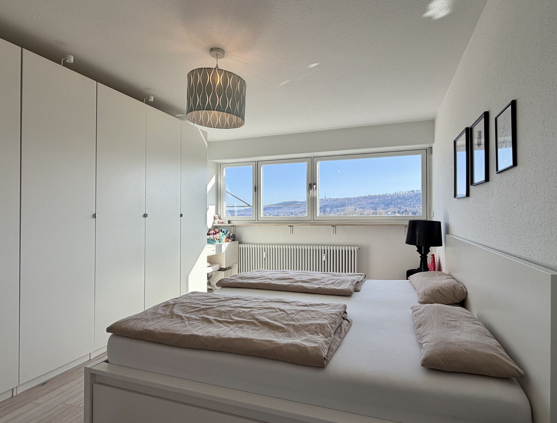 Helles Schlafzimmer mit Doppelbett, weißen Schränken und großem Fenster mit Ausblick.