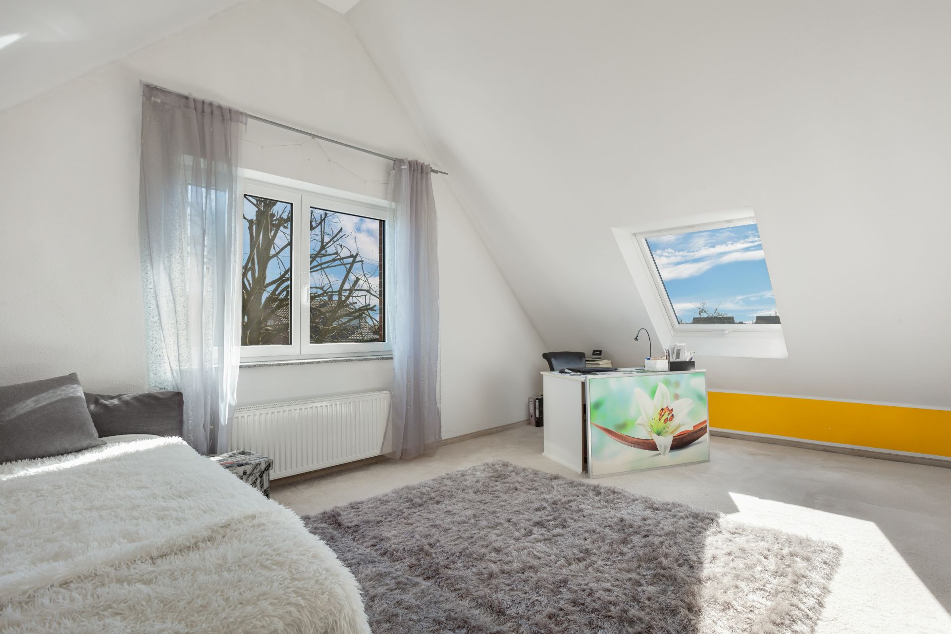 Helles Zimmer mit Dachschräge, Bett, Teppich, Schreibtisch und zwei Fenstern.