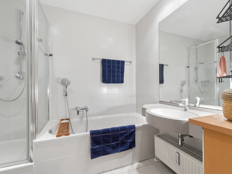 Helles Badezimmer mit Badewanne, Dusche, Waschbecken und blauen Handtüchern.