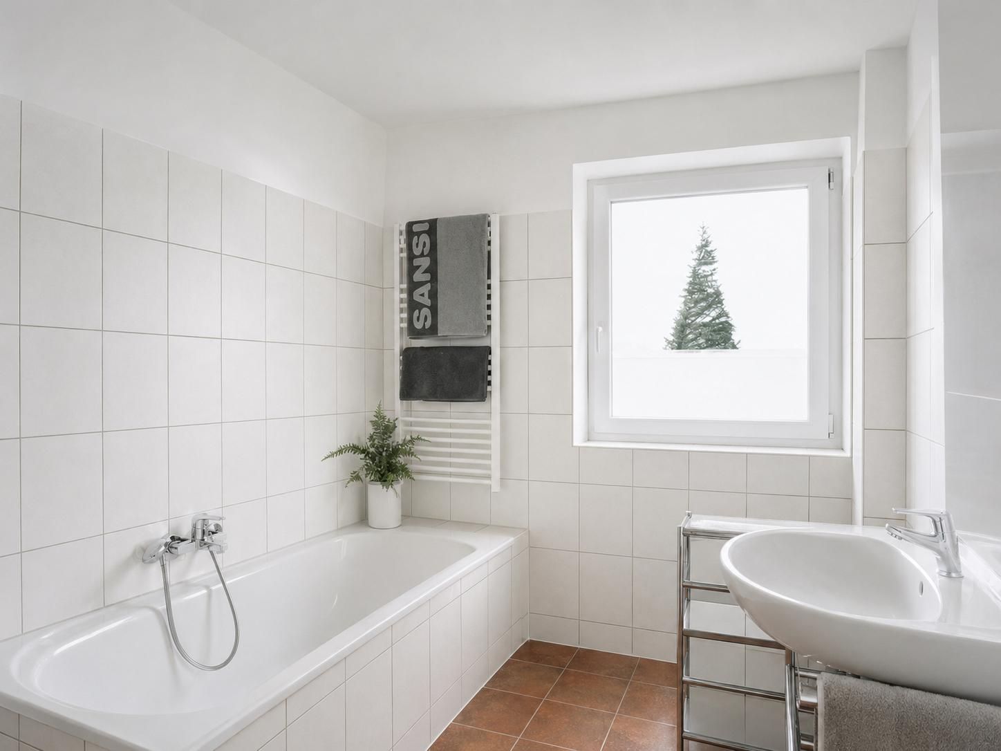 Helles Badezimmer mit Badewanne, Waschbecken, Handtuchheizkörper und Fenster.