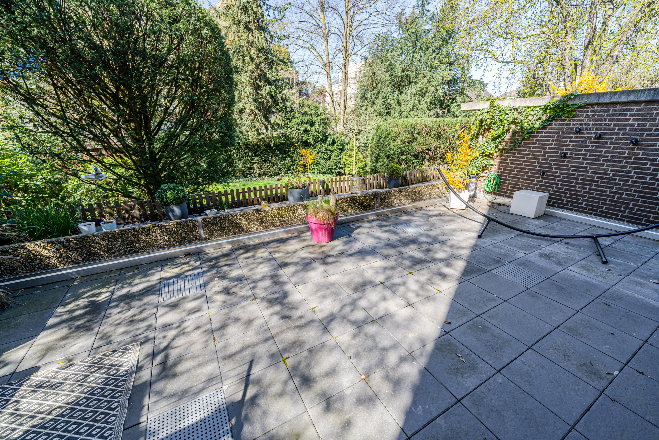 Große Terrasse mit Pflanzkübeln, Liegestuhlgestell und Blick auf Garten und Bäume.