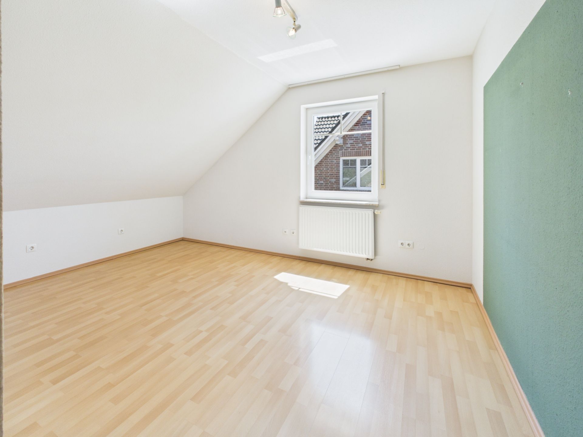Leerer Raum mit Holzfußboden, weißer Wand und Fenster unter einer Dachschräge.