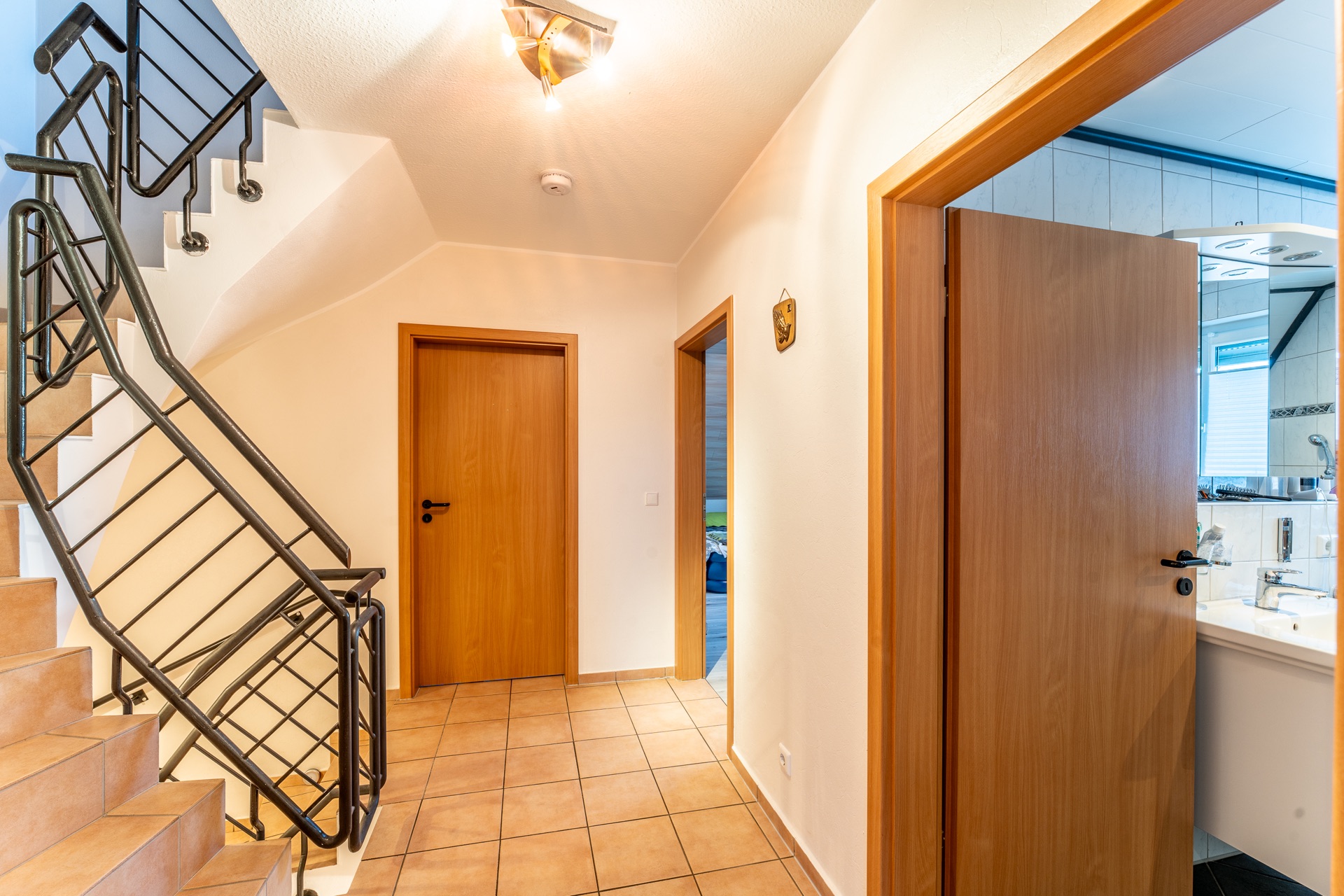 Heller Flur mit Treppe, Fliesenboden und Holztüren, rechts ist ein Badezimmer zu sehen.