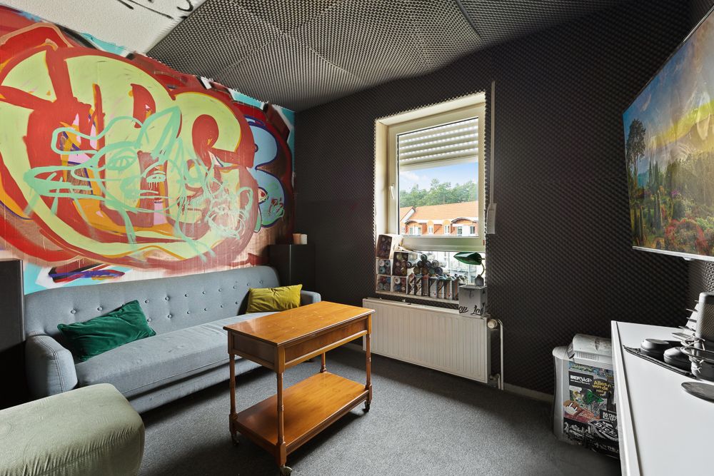 Wohnzimmer mit Sofa, Holztisch, buntem Wandbild und Fenster mit Blick nach draußen.