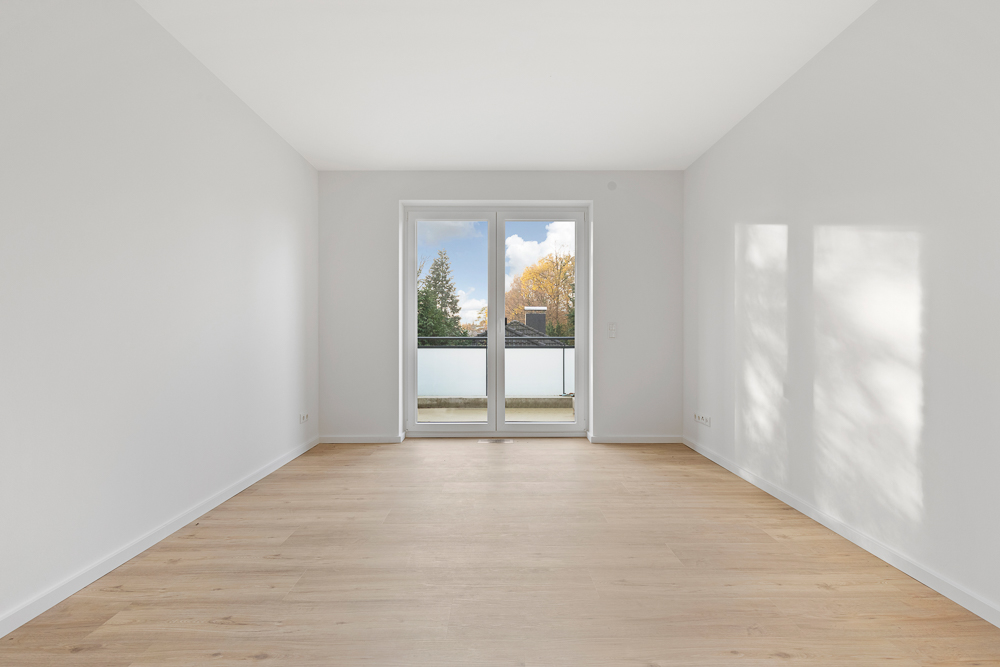 Heller, leerer Raum mit Holzboden und großen Fenstertüren zu einem Balkon.