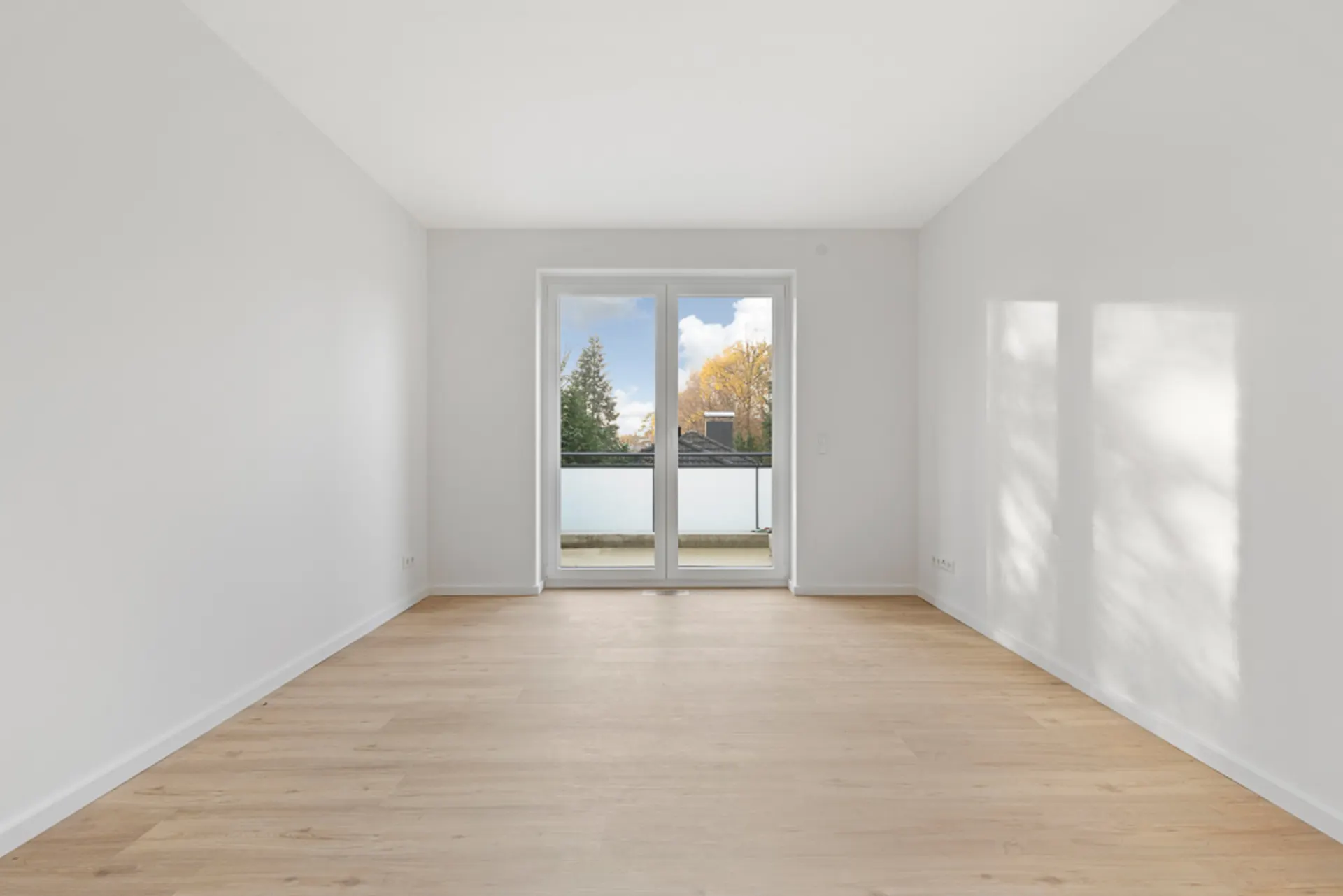 Heller, leerer Raum mit Holzboden und großen Fenstertüren zu einem Balkon.