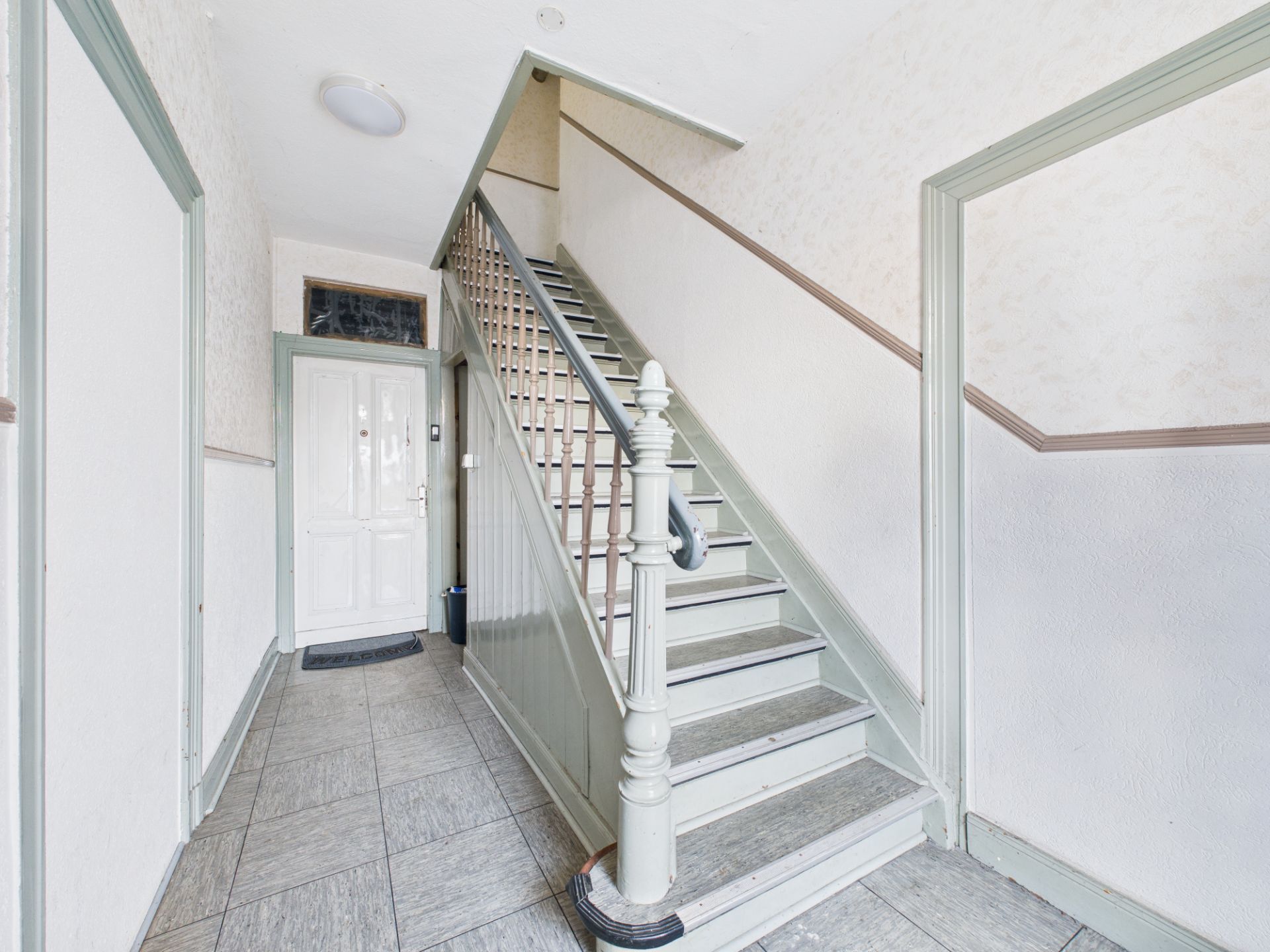 Heller Flur mit Treppe und weißer Tür in einem Wohnhaus.