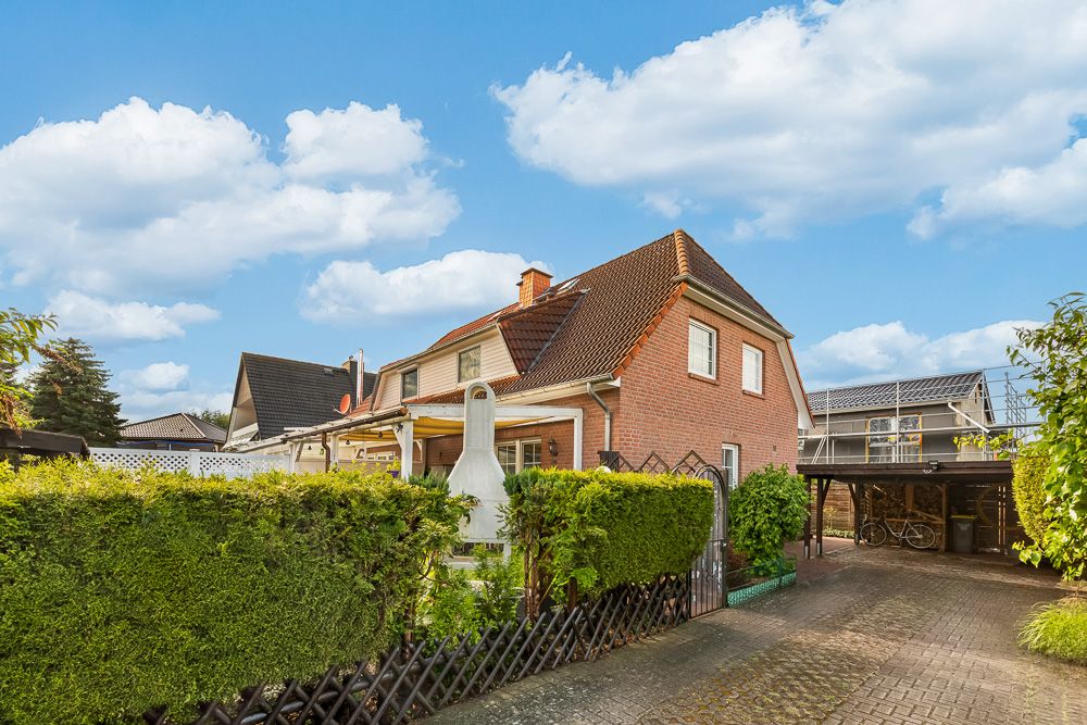 Backstein-Einfamilienhaus mit überdachter Terrasse und Carport, umgeben von Hecken.