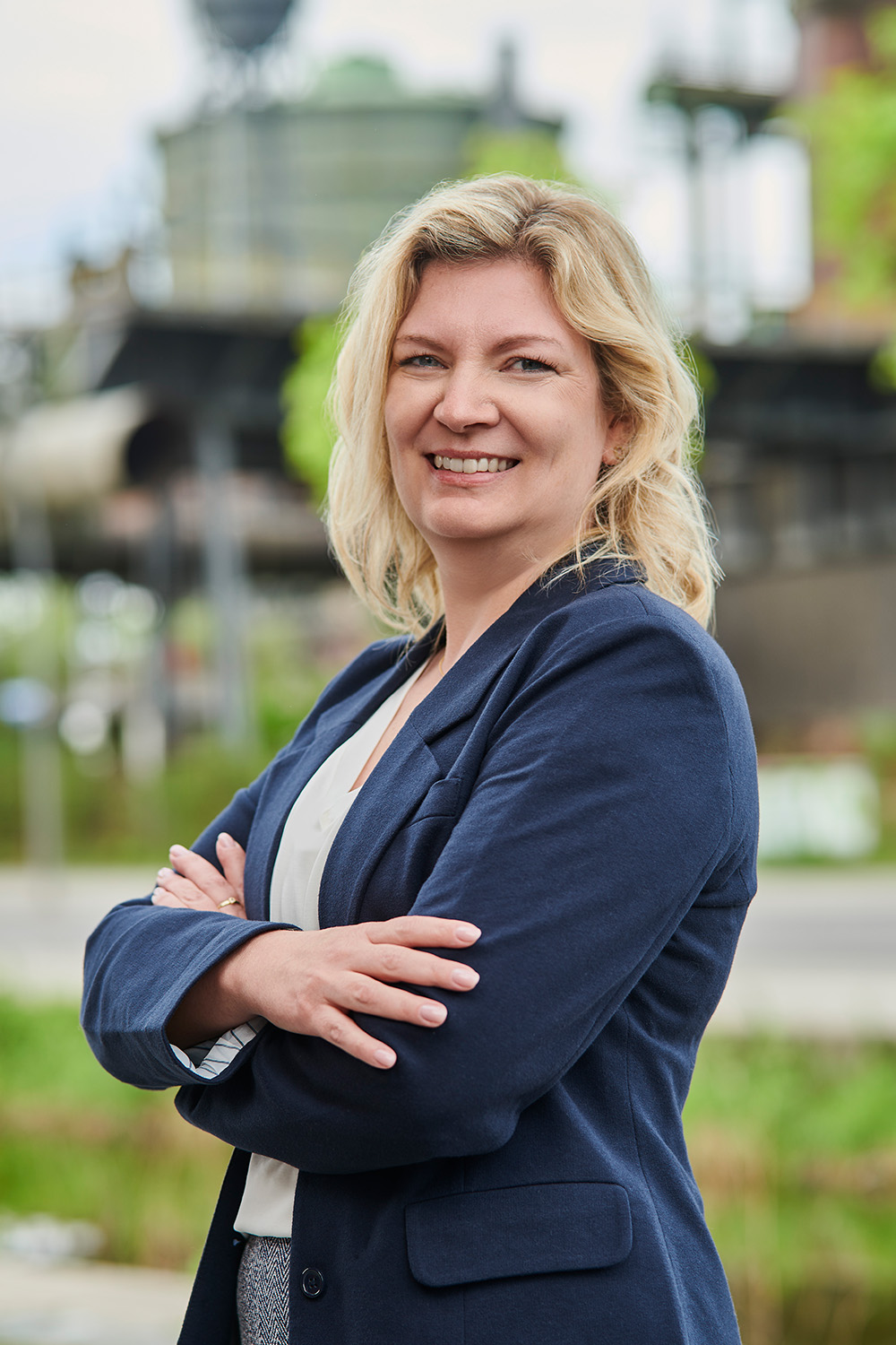 Frau mit blondem Haar und blauem Blazer steht draußen und lächelt in die Kamera.