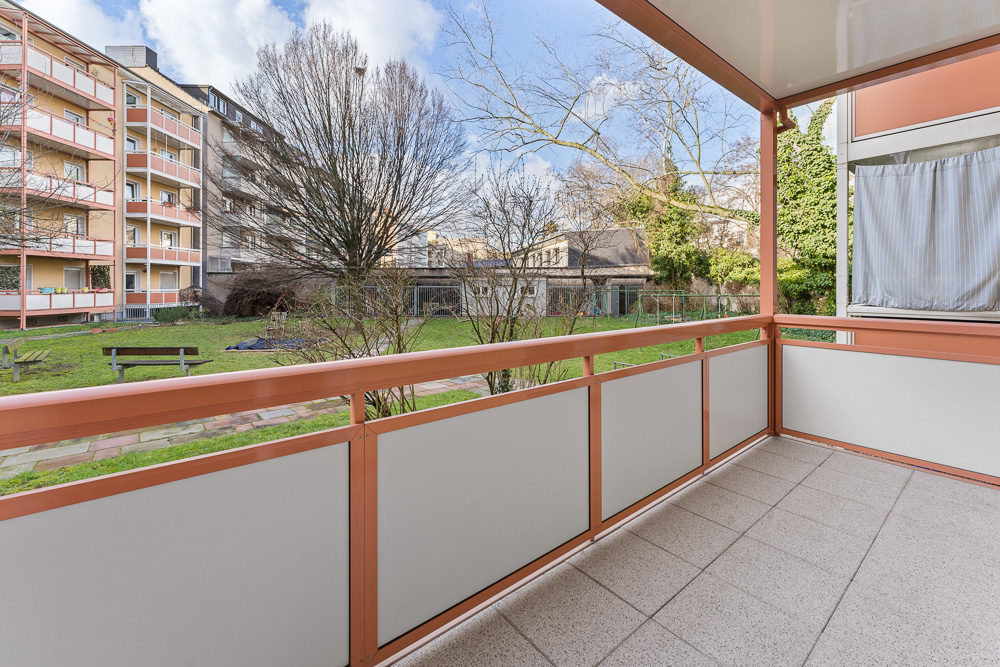 Balkon mit Blick auf einen grünen Innenhof und umliegende Wohngebäude.