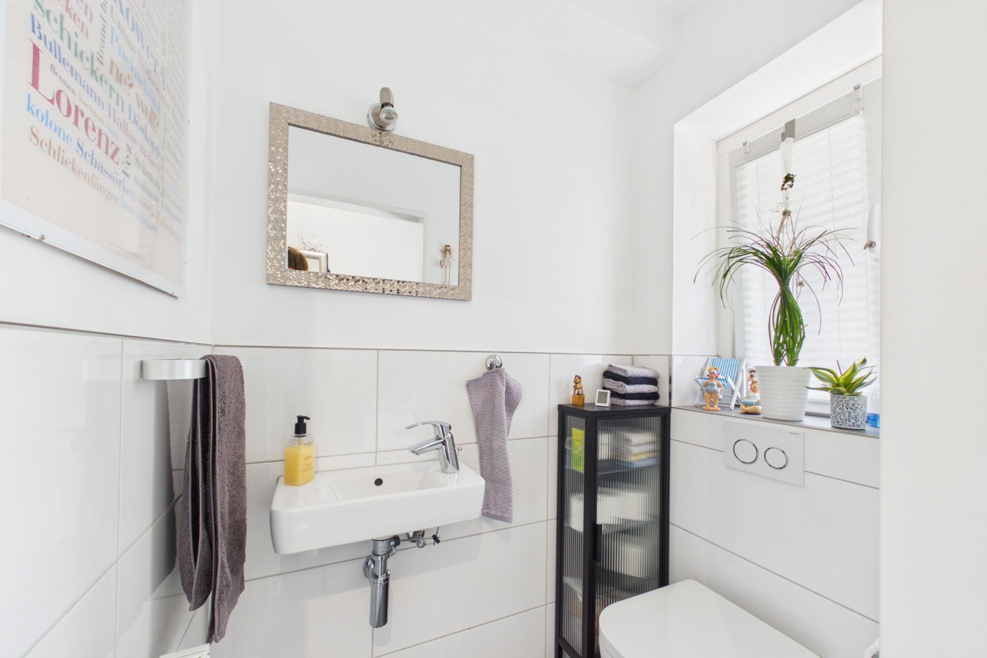 Helles Badezimmer mit Waschbecken, Spiegel, Toilette und Pflanzen auf der Fensterbank.