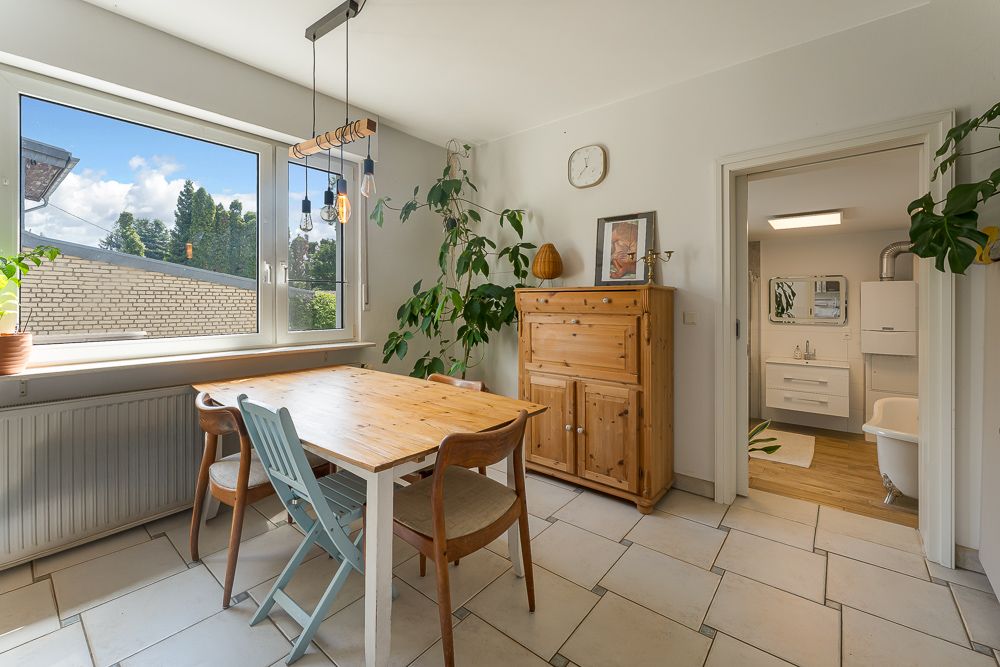 Heller Essbereich mit Holztisch, drei Stühlen, Pflanze und Blick ins Badezimmer.
